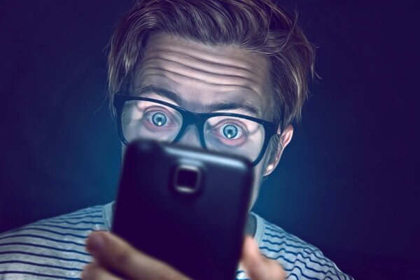 A man looking at a phone exhibiting morbid curiosity.