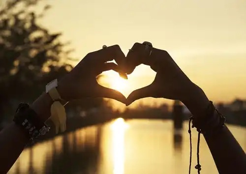 Hænder danner hjerte foran sol som symbol for sommerkærligheden