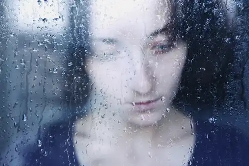 Kvinde ser ud af regnfyldt vindue og oplever lidelse
