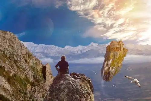 Mand sidder på klippe og ser på svævende ø med hus