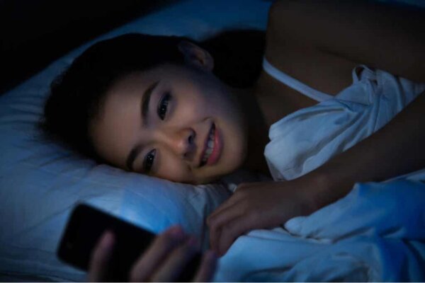 Kvinde i seng smiler over godnatbeskeder på telefonen