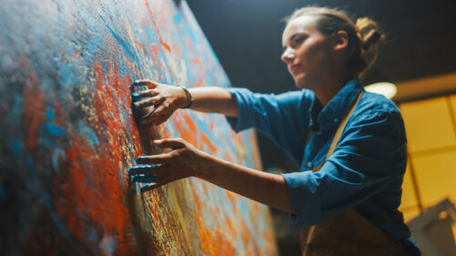 A woman painting on a large canvas with her fingers.