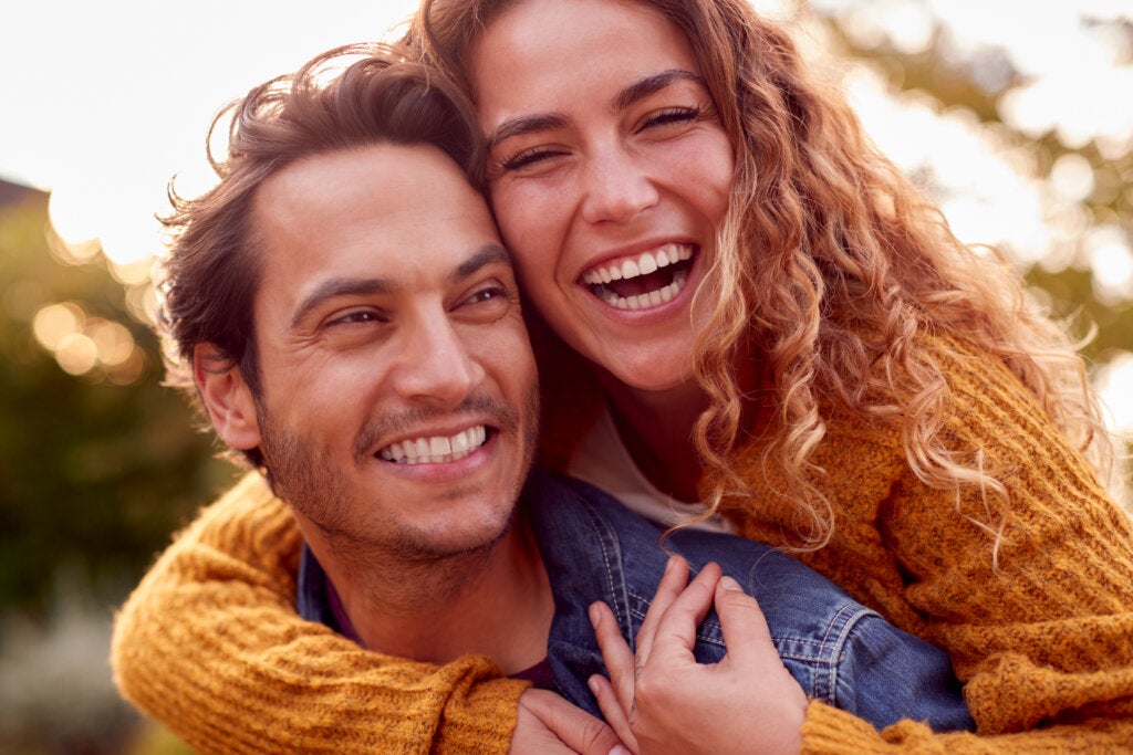 A woman hugging a man from behind while both smile.