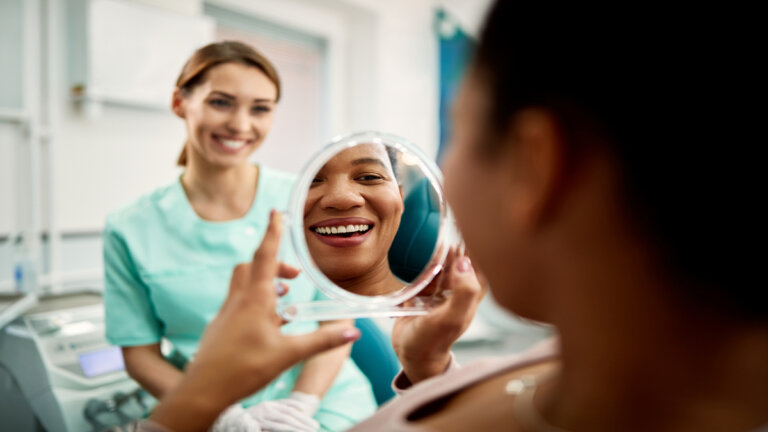 A black female patient smiling into a mirror while at the dentist.