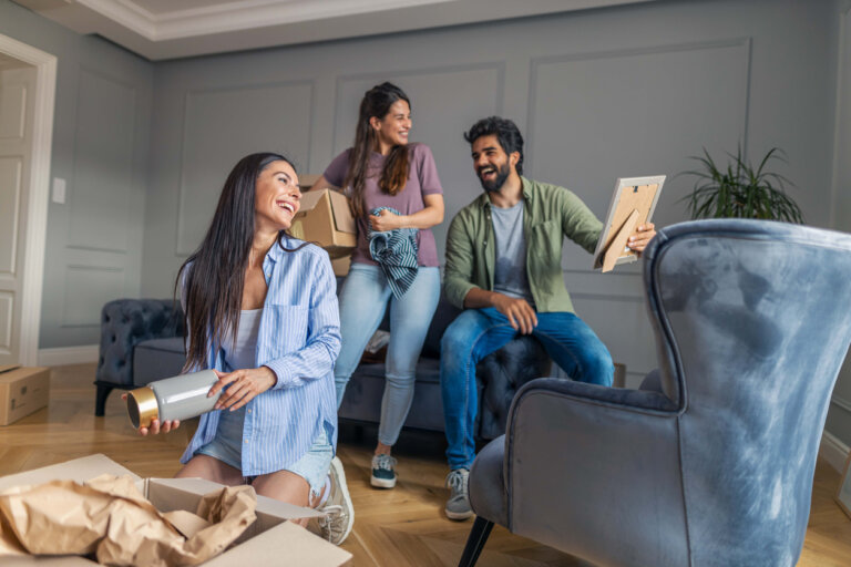 Two women and a man smiling as they move into their shared home.